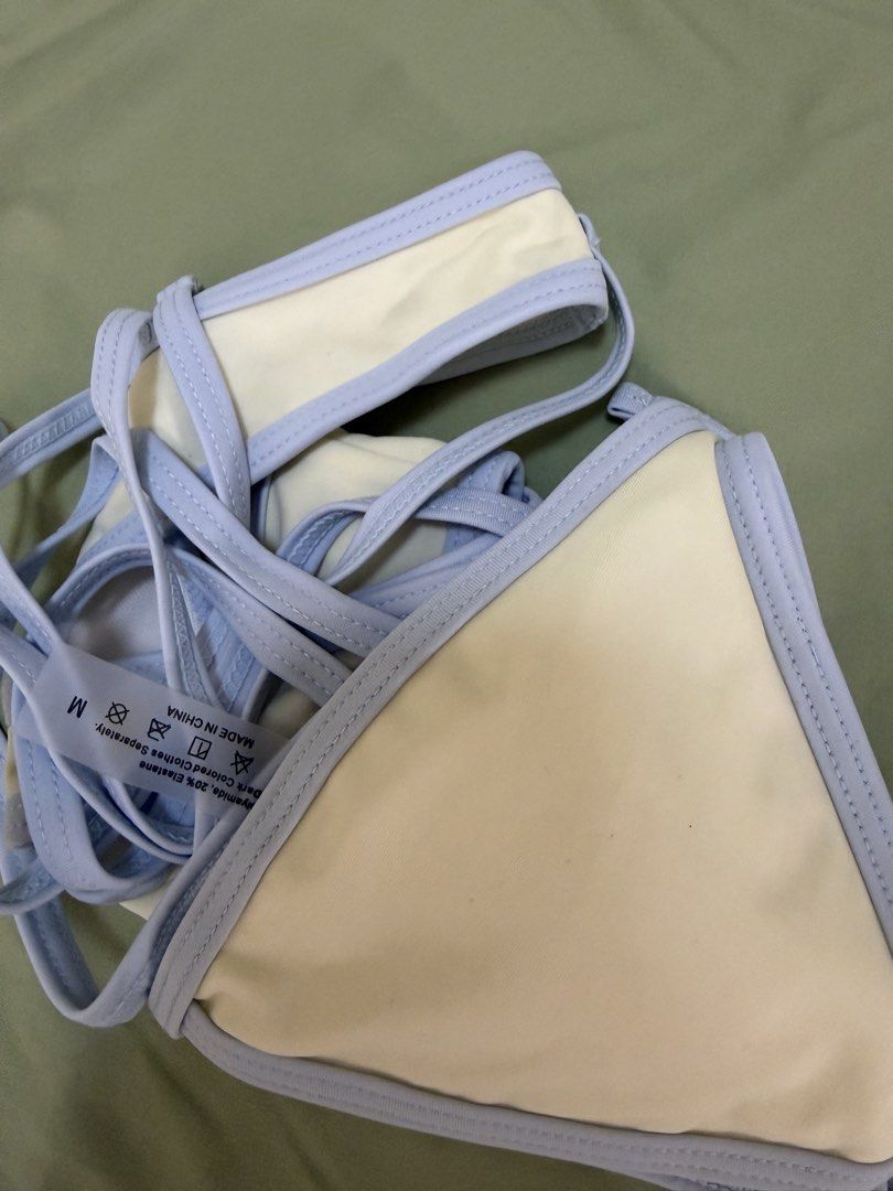 Two-piece bikini set light blue and cream (Category: Bikinis & Swimsuits) located in Makati City. Submitted by andzr. (Listing ID 1469543311, Image 3). Description: - Style: Triangle bikini top with matching high-cut, cheeky bottoms - Color: Cream with light blue trim and piping details - Size: Medium (tag attached) - Material: Polyimide and elastane blend (Made in China) - Care: Hand wash separately - Condition: Clean and neat overall.