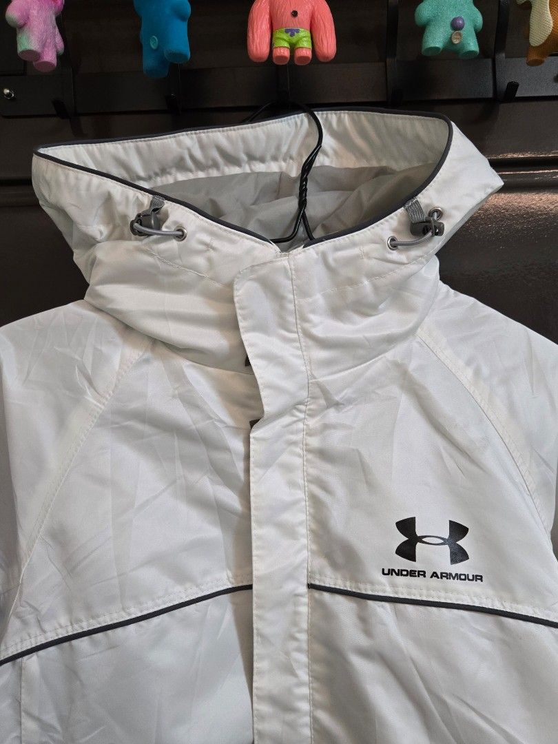 Under Armour White Hooded Windbreaker Jacket (Category: Coats, Jackets and Outerwear) located in Bulacan. Submitted by matchiii (Listing ID 1469529854, Image 2). Description: - Color: White with grey fleece inner lining - Size: Large (L) - Closure: Full zip with velcro storm flap - Hood: Adjustable with drawstring and printed logo - Pockets: Convenient side zippered pockets - Cuffs: Elastic with adjustable velcro straps - in good condition.