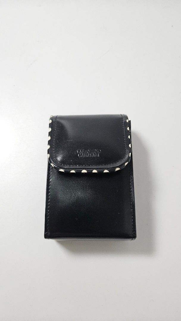 Valentino Garavani Black Leather Cigarette Case (Category: Wallets & Card Holders) located in Alfonso. Submitted by jbcamet (Listing ID 1469513404, Image 1). Description: - Brand: Valentino Garavani - Material: Black leather with stamped logo on front and inside - Closure: Flap with secure snap button - Capacity: Designed to securely hold one standard pack of cigarettes - Condition: Shows visible scuffs and surface wear on the exterior, priced ac
