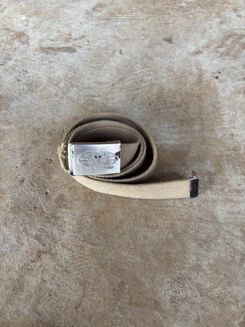 Vintage Alien Workshop Belt (Category: Belts) located in Puerto Princesa. Submitted by 18arc (Listing ID 1469512701, Image 1). Description: • Brand: Alien Workshop (off/legit)(skateboarding/streetwear brand) • Style: Military-style web belt with a flip-tab plaque buckle • Material: Khaki/beige cotton or canvas webbing with a metal tip and buckle • Era: 1990s (Y2K / vintage skate collectible).