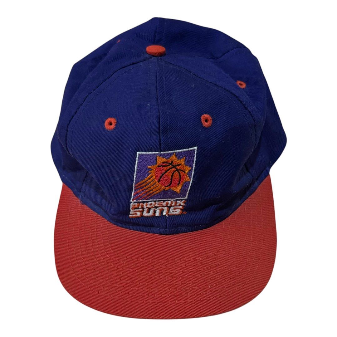 Vintage Phoenix Suns Snapback Cap (Category: Caps & Hats) located in Maragusan (San Mariano). Submitted by dripdrops_ddo (Listing ID 1469553257, Image 3). Description: - Official 90s NBA licensed Phoenix Suns snapback by Competito - Deep blue crown with contrasting red flat brim and top button - Embroidered team logo patch on the front - Bold orange 'PHOENIX' lettering embroidered on the back arch - Red adjustable snap closure (One Size Fits All)