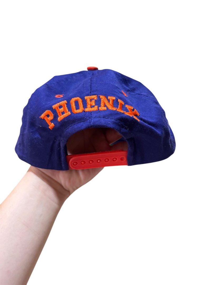 Vintage Phoenix Suns Snapback Cap (Category: Caps & Hats) located in Maragusan (San Mariano). Submitted by dripdrops_ddo (Listing ID 1469553257, Image 2). Description: - Official 90s NBA licensed Phoenix Suns snapback by Competito - Deep blue crown with contrasting red flat brim and top button - Embroidered team logo patch on the front - Bold orange 'PHOENIX' lettering embroidered on the back arch - Red adjustable snap closure (One Size Fits All)