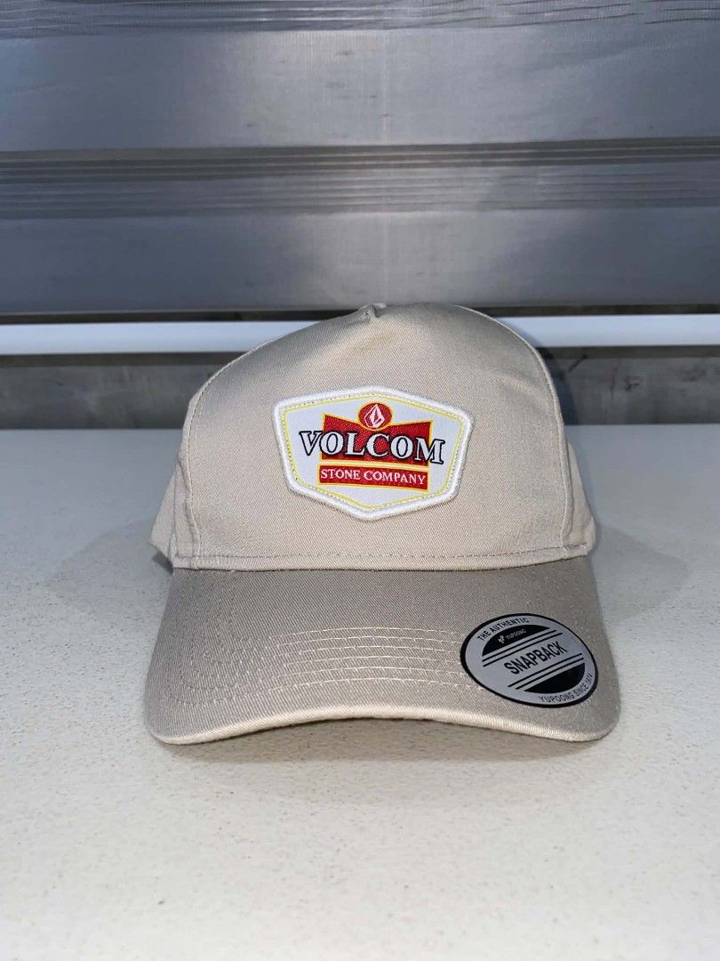 Volcom Stone Company Snapback Cap Beige (Category: Caps & Hats) located in Baler. Submitted by mariokush193815 (Listing ID 1469453415, Image 1). Description: - Brand: Volcom Stone Company - Color: Classic Beige - Condition: Brand new with sticker still attached on the brim - Design: Structured crown with a curved brim - Details: Embroidered Volcom logo patch on the front - Closure: Adjustable plastic snapback with small logo tag - Fit: One Size F