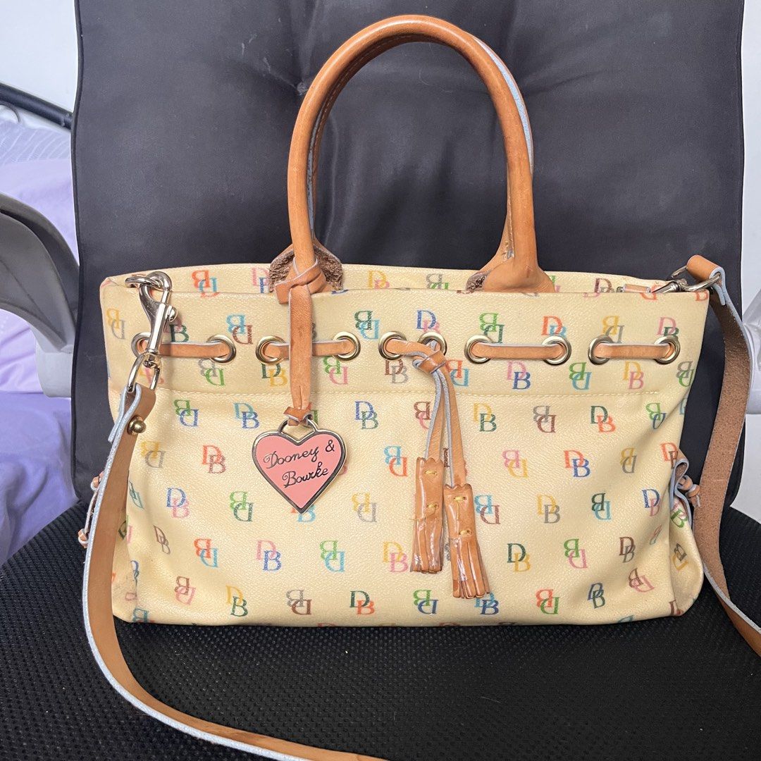 🇺🇸 Dooney & Bourke Multicolored DB Monogram Yellow Handbag (Category: Luxury Bags & Wallets) located in Manila. Submitted by prelovedpick.com (Listing ID 1469594492, Image 1). Description: With Freebies - Brand: Dooney & Bourke - Color: Cream with multicolored DB monogram print - Material: Coated canvas with tan leather trim - Straps: Top handles and a detachable shoulder strap - Hardware: Gold-tone with pink enamel heart charm - Details: Draws