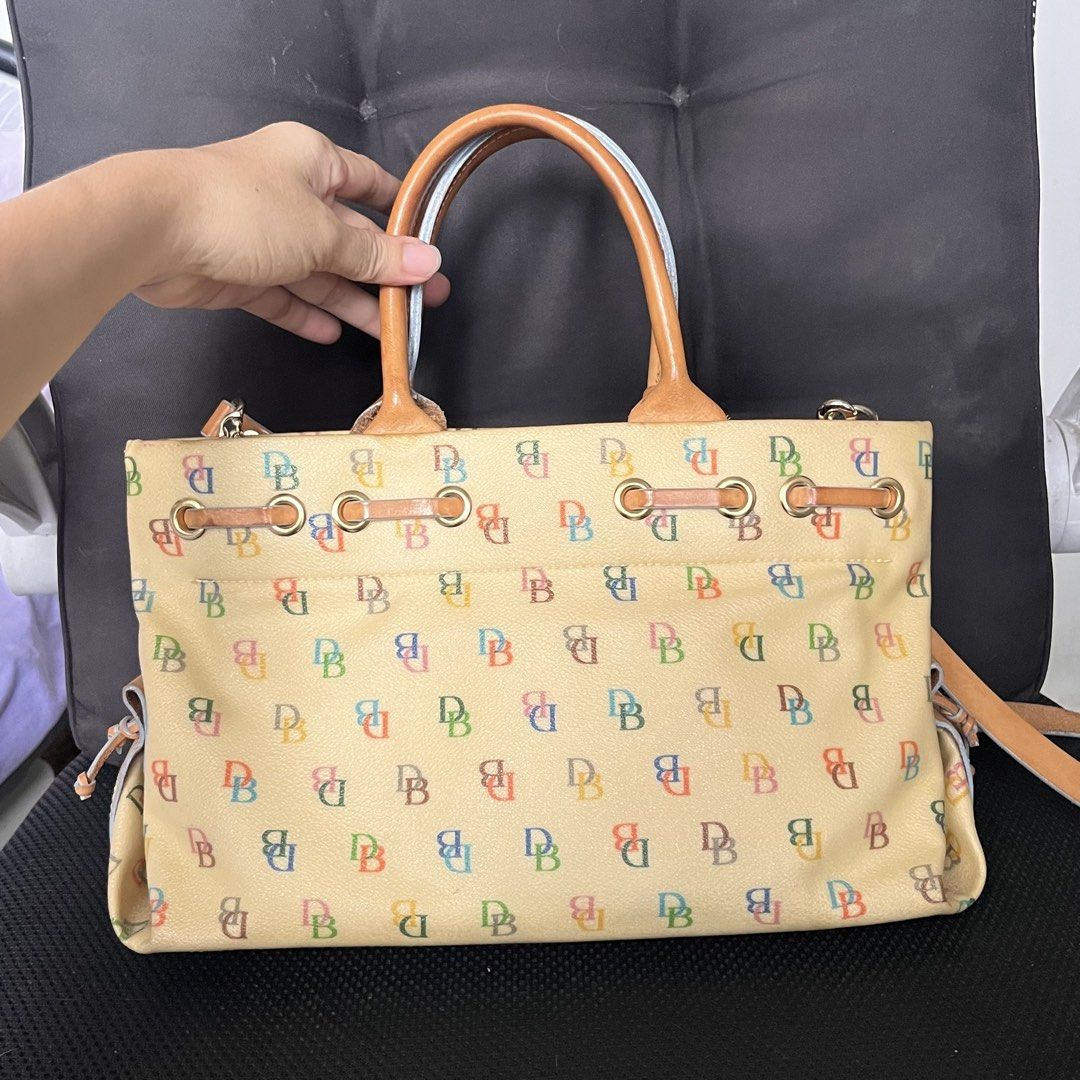 🇺🇸 Dooney & Bourke Multicolored DB Monogram Yellow Handbag (Category: Luxury Bags & Wallets) located in Manila. Submitted by prelovedpick.com (Listing ID 1469594492, Image 2). Description: With Freebies - Brand: Dooney & Bourke - Color: Cream with multicolored DB monogram print - Material: Coated canvas with tan leather trim - Straps: Top handles and a detachable shoulder strap - Hardware: Gold-tone with pink enamel heart charm - Details: Draws