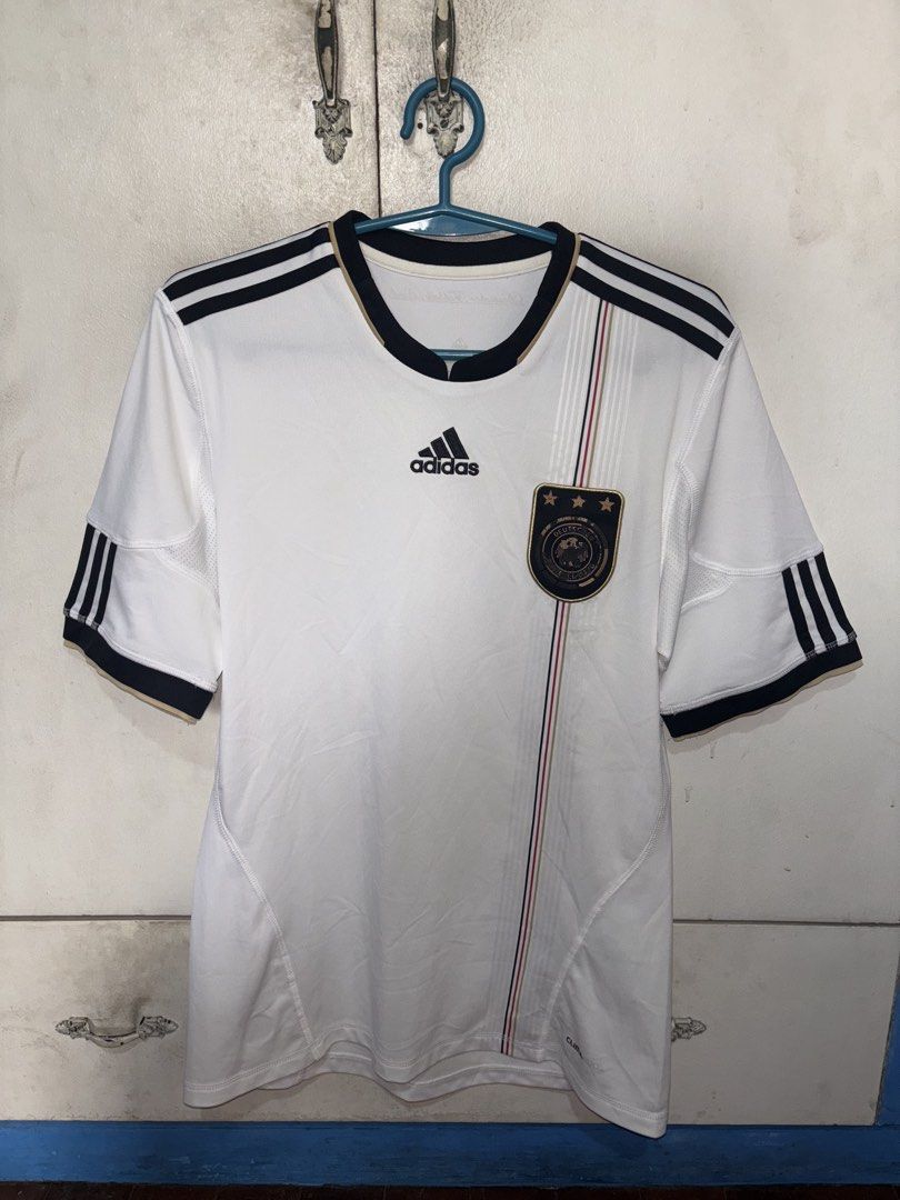 Adidas Germany 2010/2011 Home Kit (Category: Activewear) located in Pasig City. Submitted by timmybatoon (Listing ID 1469601379, Image 1). Description: - Classic white home jersey from Germany's iconic 2006 World Cup campaign - Features the striking black, red, and gold vertical stripe down the front - Embroidered Adidas logo and DFB crest with 3 championship stars - Deutscher Fußball-Bund lettering on the back collar - Climacool technology for b