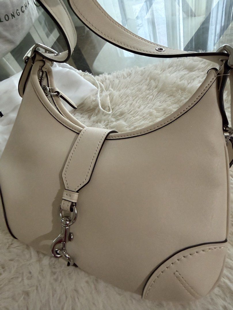 Authentic Coach Hampton Hobo Bag (Category: Luxury Bags & Wallets) located in Manila. Submitted by bagluxeph (Listing ID 1469711298, Image 2). Description: - Brand: Coach - Color: Off-white - Material: Genuine leather with brown leather interior - Hardware: Silver-tone - Closure: Dog leash clip - Strap: Adjustable with buckle detail - Interior: Features official Coach creed patch - Inclusions: Dust bag included Used once - Like new condition.