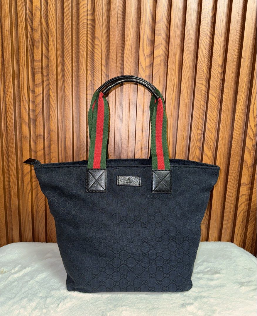 Authentic Gucci Monogram Canvas Tote Bag Black (Category: Everything Else Others) located in Subic. Submitted by luxshoppe88 (Listing ID 1469700627, Image 1). Description: Black canvas tote bag with iconic GG monogram pattern all over. Web stripe handles in red and green with black leather trim. Secure top zip closure and sturdy leather bottom base. Interior lined in black fabric with an extra slip pocket. Spacious design holds all daily essentia