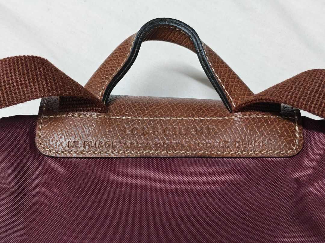 Authentic Longchamp Le Pliage Sac A Dos Backpack Plum (Category: Backpacks) located in Pasig City. Submitted by she_declutters_ph (Listing ID 1469645268, Image 2). Description: - Brand: Longchamp Le Pliage Backpack - Color: Plum with signature brown leather flap and top handle - Material: Durable nylon body with adjustable webbed shoulder straps - Design: Folds down into a compact size for easy storage - Closure: Front flap with snap button - Use