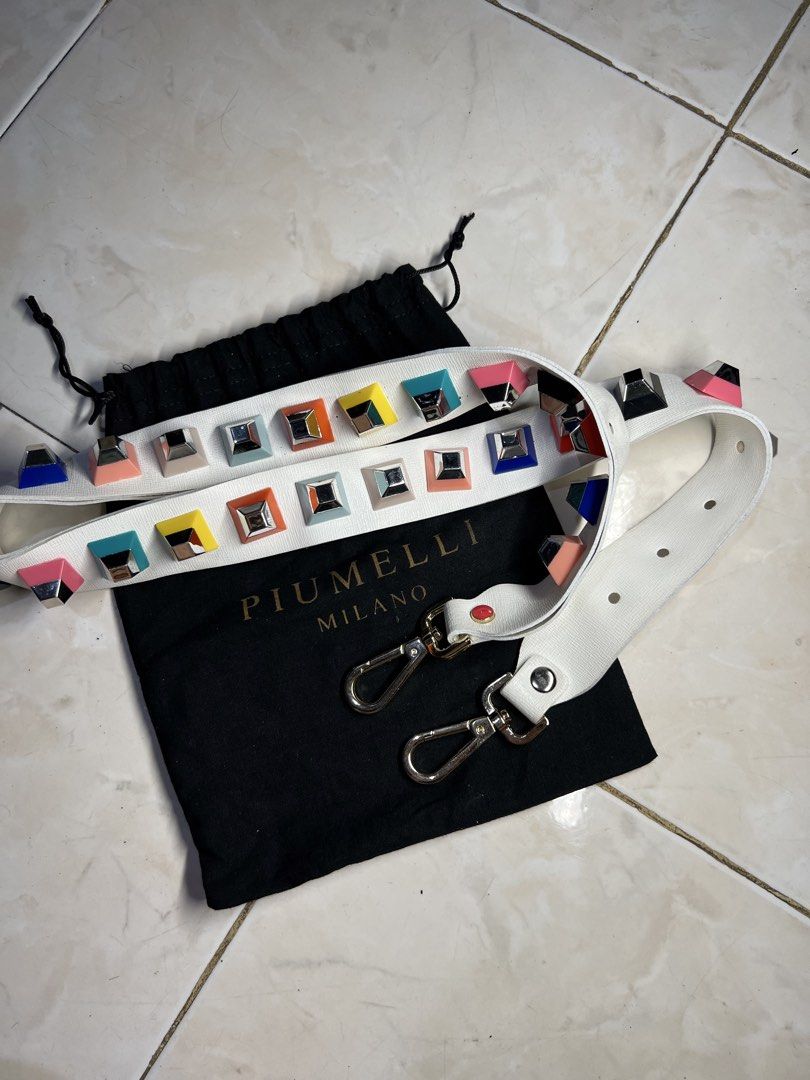 AUTHENTIC PIUMELLI Milano multi-color block studded decorative bag strap (Category: Luxury Bags & Wallets) located in General Santos City (Dadiangas). Submitted by queenfinds (Listing ID 1469720936, Image 2). Description: Piumelli Milano multi-color block studded decorative bag strap, displayed alongside its original gold-stamped black flannel dust bag. This piece features a premium white leather body adorned with two parallel rows of vibrant, mu