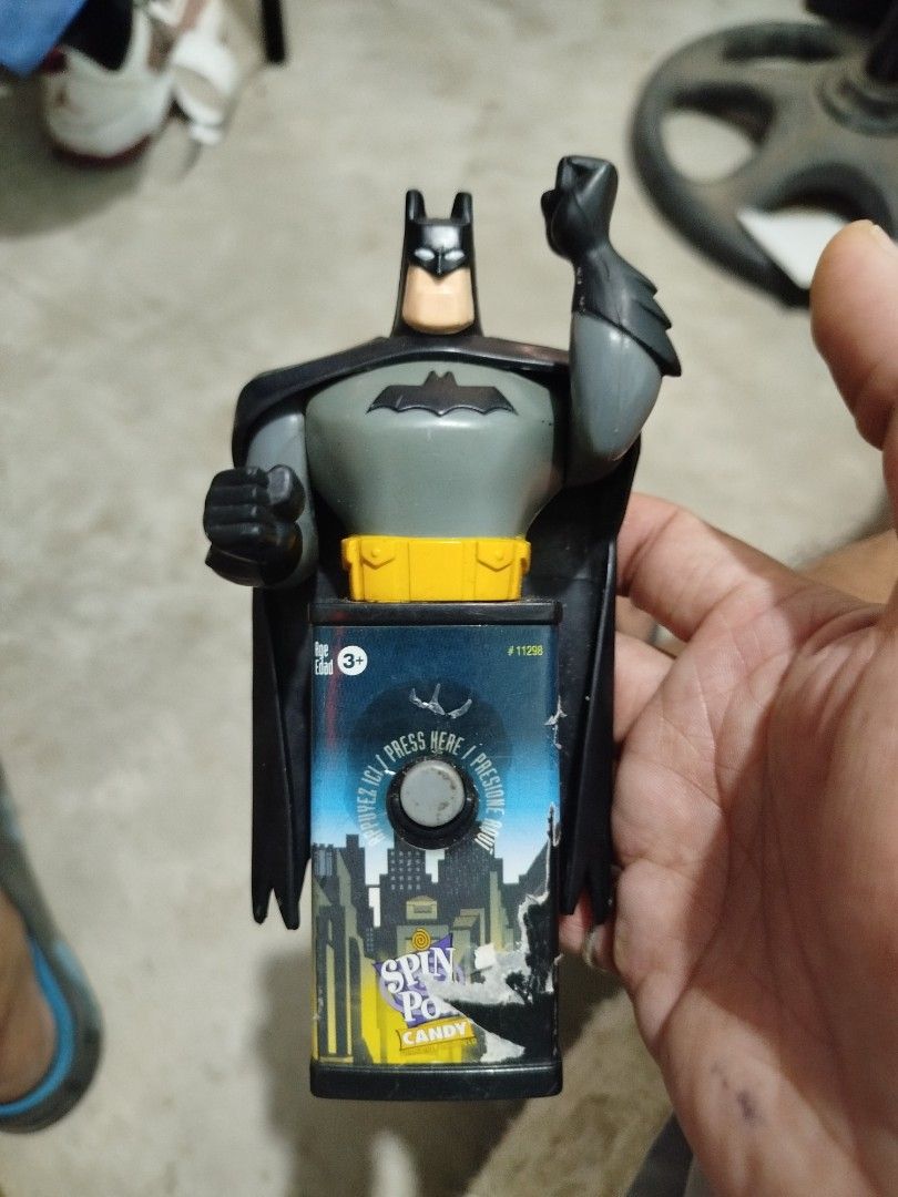 Batman Spin Pop Candy Dispenser Figure (Category: Figurines & Statues) located in Subic. Submitted by regiedaniel01 (Listing ID 1469580856, Image 1). Description: - Batman figure with a candy dispenser base - Features a Gotham City graphic on the front with a push button - Attached black cape and iconic yellow utility belt - Minor wear and peeling on the bottom paper label - Overall solid shape, perfect for display.