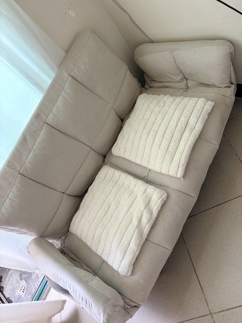 Beige foldable sofa bed with wooden legs (Category: Sofas) located in Makati City. Submitted by makatigirlpreloved (Listing ID 1469618608, Image 2). Description: - Beige tufted fabric sofa bed, adjustable backrest folds down completely flat. - discoloration and stains visible on the fabric surface, plus light scuff marks on the wooden legs. - selling with throw pillow .