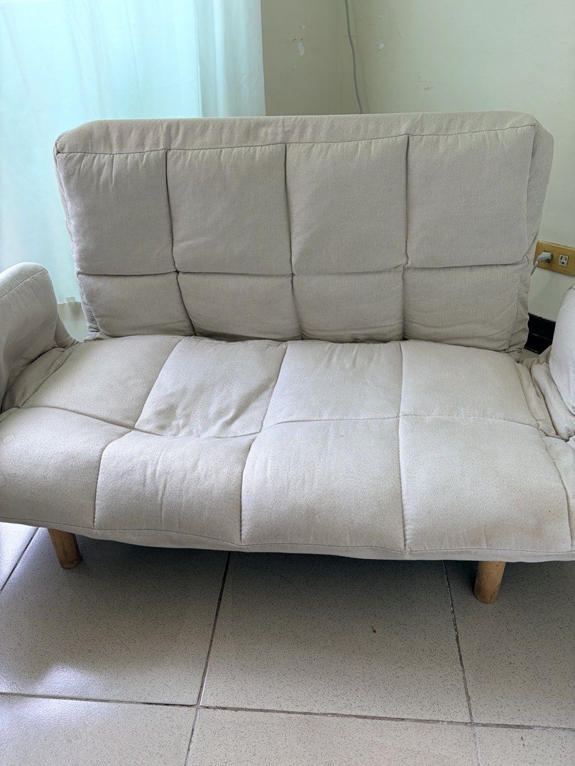 Beige foldable sofa bed with wooden legs (Category: Sofas) located in Makati City. Submitted by makatigirlpreloved (Listing ID 1469618608, Image 1). Description: - Beige tufted fabric sofa bed, adjustable backrest folds down completely flat. - discoloration and stains visible on the fabric surface, plus light scuff marks on the wooden legs. - selling with throw pillow .