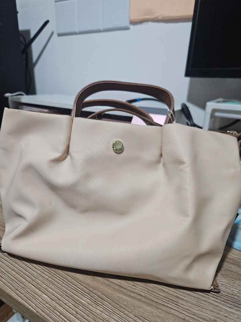 Beige Nylon Handbag with Brown Handles (Category: Tote Bags) located in Pasay City. Submitted by chichaarown (Listing ID 1469670748, Image 1). Description: - Color: Versatile beige with brown leather-look handles and trim - Material: Durable nylon with gold-tone hardware - Closure: Secure top zipper with a stylish front flap button accent - Design: Soft, unstructured body with a roomy interior - Perfect for daily use and matches any outfit.