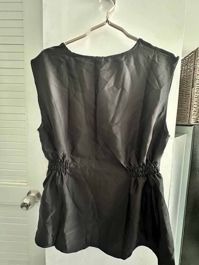 BKK Black Sleeveless Ruched Blouse Top (Category: Sleeveless) located in Taguig. Submitted by sherylannc (Listing ID 1469626494, Image 3). Description: - Brand: BKK (Brand New With Tag) - Color: Sleek black with a smooth, slight-sheen fabric - Fit: Relaxed upper body with gathered elastic sides for a defined waist - Design: Round neckline, flared hem, and trendy asymmetric side draping - Versatility: Perfect for both casual days and dressy night 