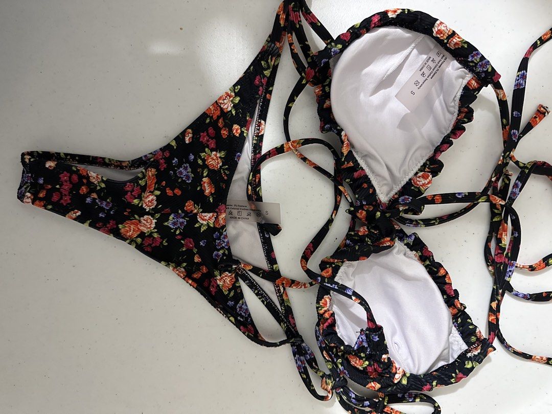 Black Floral Print Ruffle Bikini Set Size S (Category: Bikinis & Swimsuits) located in Pasig City. Submitted by prelovedbysco (Listing ID 1469592544, Image 3). Description: - Condition: Brand new with tags (BNWT) - Size: Small (S) - Design: Colorful rose and floral print on ribbed textured fabric - Top: Ruffled trim edges with adjustable string ties - Bottoms: Side tie straps with a cheeky cut - Material: Polyester and elastane with white inner l
