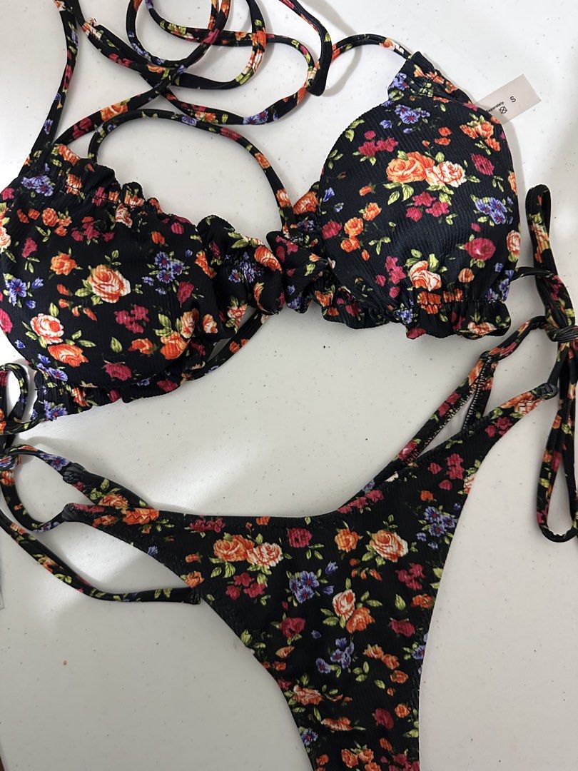 Black Floral Print Ruffle Bikini Set Size S (Category: Bikinis & Swimsuits) located in Pasig City. Submitted by prelovedbysco (Listing ID 1469592544, Image 2). Description: - Condition: Brand new with tags (BNWT) - Size: Small (S) - Design: Colorful rose and floral print on ribbed textured fabric - Top: Ruffled trim edges with adjustable string ties - Bottoms: Side tie straps with a cheeky cut - Material: Polyester and elastane with white inner l