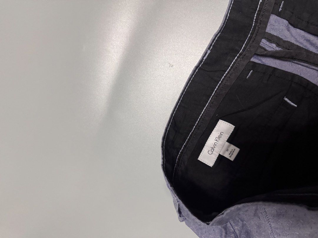 Calvin Klein Grey Blue Shorts Size 32 (Category: Shorts) located in Alaminos. Submitted by outfitcheck.ph (Listing ID 1469698072, Image 3). Description: - Brand: Calvin Klein - Size: Men's 32 - Color: Blue-Grey - Closure: Standard button and zip with belt loops - Pockets: Two front pockets and two back welt pockets - Details: Subtle metal logo badge on the right back pocket - Condition: Clean inside lining with printed brand label.