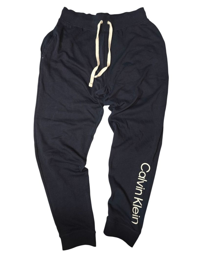 Calvin Klein Navy Logo Sweatpants (Category: Joggers) located in Baguio. Submitted by boneteezandharmony (Listing ID 1469663367, Image 2). Description: Minimalist navy blue Calvin Klein sweatpants featuring bold contrast branding along the leg, cream drawstrings, and ribbed waistband and ankle cuffs. A clean, comfortable piece for casual everyday fits. Tagged Calvin Klein Sleepwear, made in Bangladesh. Condition: 8/10 Dimes: 15 × 39 .