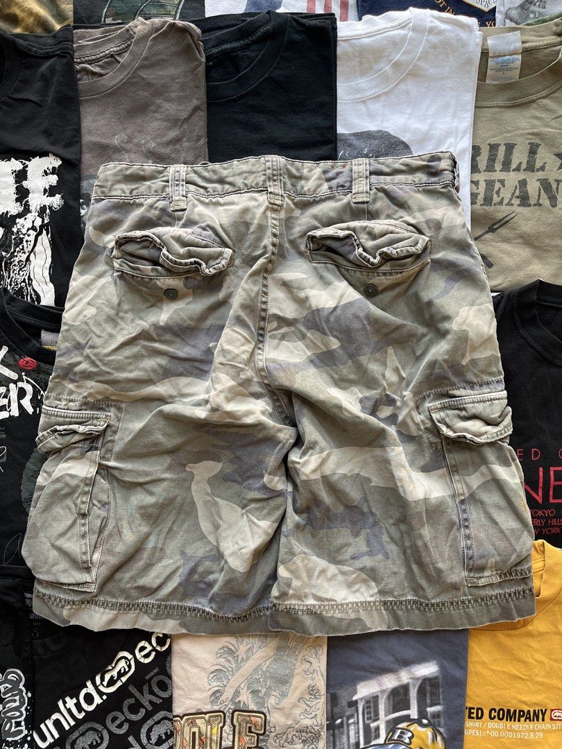 Cargo Supply Camouflage Cargo Shorts (Category: Shorts) located in Baao. Submitted by plainclothesdept (Listing ID 1469696906, Image 2). Description: cargo supply camo cargo shorts waist - 34 in. length - 21 in. hem - 12 in. paint stains, signs of wear - Brand: Cargo Supply - Design: Grey and white camo pattern with a cool red inner waistband detail - Closure: Classic button fly - Storage: Multiple side cargo pockets plus standard front and back 