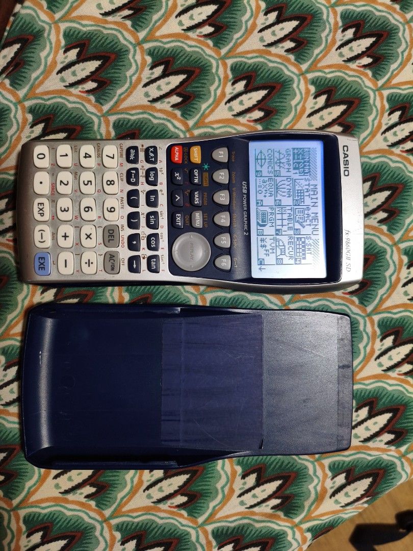 Casio fx-9860GII SD Graphing Calculator (Category: Office & Business Technology) located in Lubao. Submitted by aczcollectibles (Listing ID 1469616888, Image 1). Description: Casio fx-9860GII SD graphing calculator in working condition. Screen turns on and displays the main menu clearly. Buttons are all intact with legible text markings. Includes the hard protective slide cover. Standard scientific and graphing functions available. Battery compar