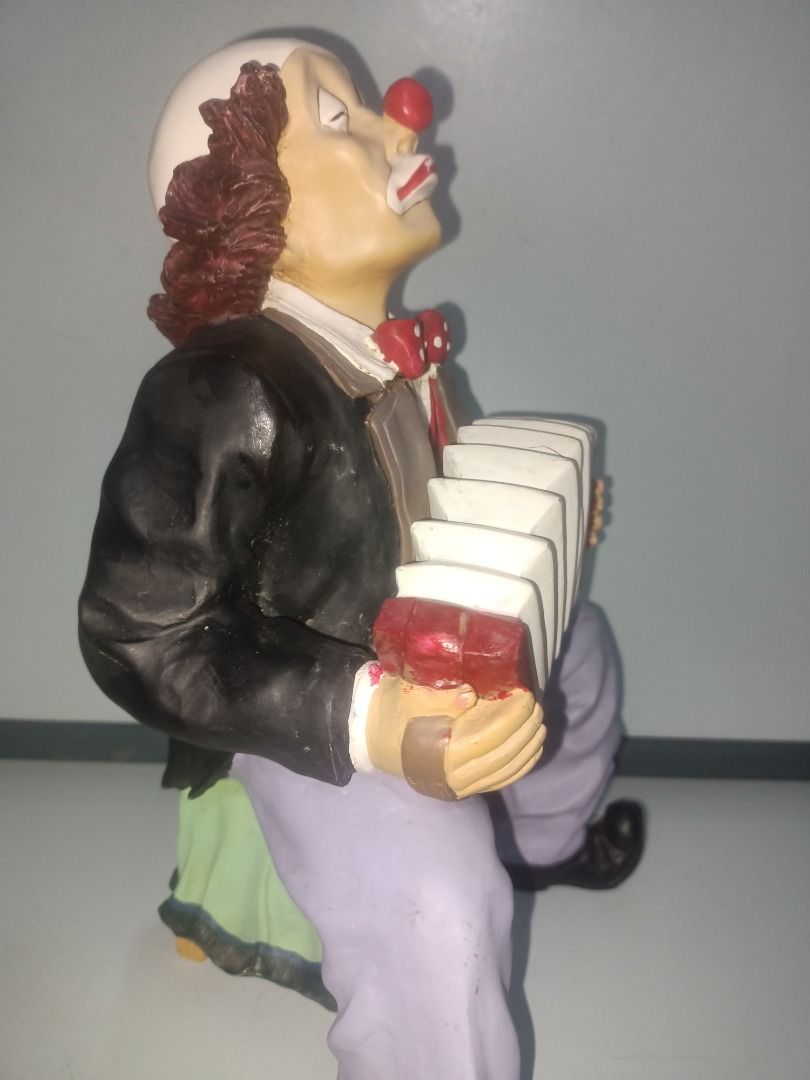 Clown playing accordion figurine (Category: Figurines & Statues) located in Munoz. Submitted by larryc1212 (Listing ID 1469678044, Image 3). Description: - Type: Clown statue playing an accordion - Size: Roughly 9.75 inches tall - Design: Detailed face paint, red nose, white makeup, and brown frizzy hair - Outfit: Black jacket, white shirt, polka dot bow tie, and light purple pants, seated on a green base - Condition: Good shelf decor - Ideal for