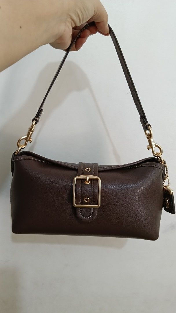 Coach Abbie Shoulder Bag with Buckle (Category: Luxury Bags & Wallets) located in Cebu City. Submitted by mcmapio (Listing ID 1469622555, Image 1). Description: - Authentic Coach shoulder bag in dark brown leather - with long strap, can be worn as sling bag - Elegant gold-tone hardware with center buckle detail - Includes matching leather charm with iconic horse and carriage logo - Dark fabric-lined interior featuring a slip pocket and Coach cree