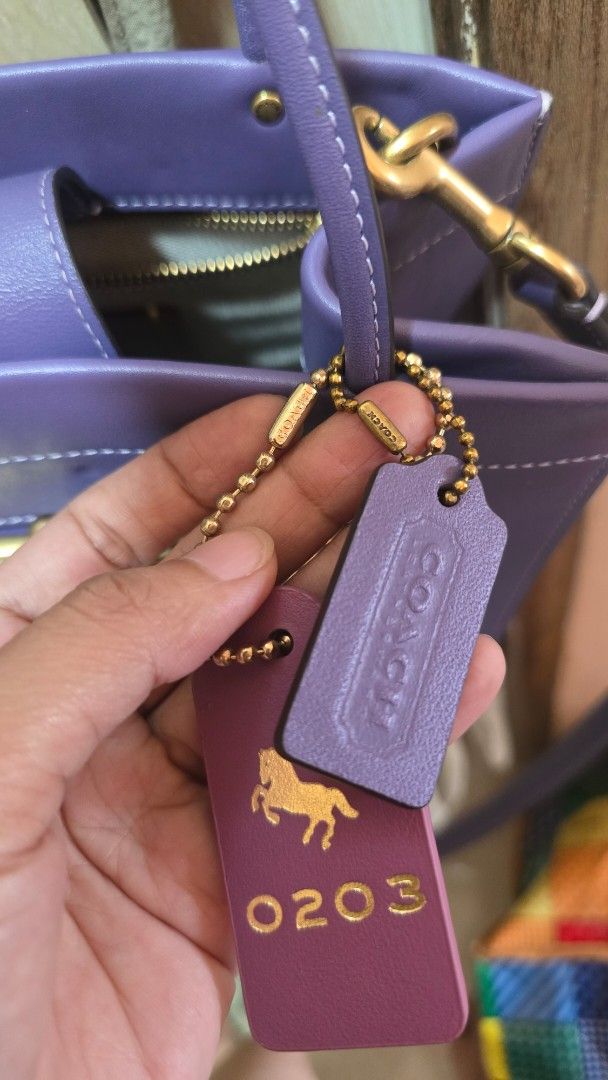 Coach Purple Leather Handbag with Gold Hardware (Category: Luxury Bags & Wallets) located in Quezon City. Submitted by mbpreloved65 (Listing ID 1469656776, Image 2). Description: - Brand: Coach - Material: Premium purple leather with brass-tone hardware - Design: Double gold clasp frames on the front - Extras: Matching purple leather hangtags, including one embossed with the horse and carriage logo and number 0203 - Carry options: Double top hand