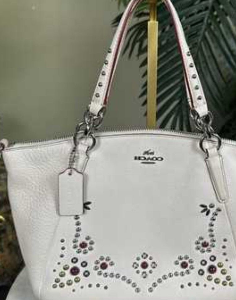 Coach White Leather Studded Handbag Shoulder Bag (Category: Cross-body Bags) located in Manila. Submitted by lene48 (Listing ID 1469649612, Image 1). Description: - Authentic Coach white pebbled leather bag - Silver-tone hardware with secure zipper closure - Unique front panel accented with metal studs and colorful stones - Dual top handles and a convenient detachable long strap - Classic Coach leather hangtag included - Clean back side with a ch