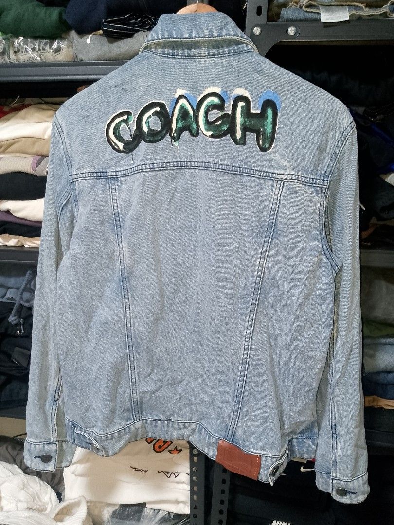 Coach x Mint + Serf Denim Jacket (Category: Coats, Jackets and Outerwear) located in Manila. Submitted by mjthrifted_second (Listing ID 1469635089, Image 2). Description: - Brand: Coach x Mint + Serf - Style: Light wash blue denim jacket with graffiti Coach logo on the back - Size: Small (Regular fit) -Dimes: 20/25 - Material: 100% cotton body with cow leather trim on the back hem patch - Features: Metal button closure, dual chest pockets, and si