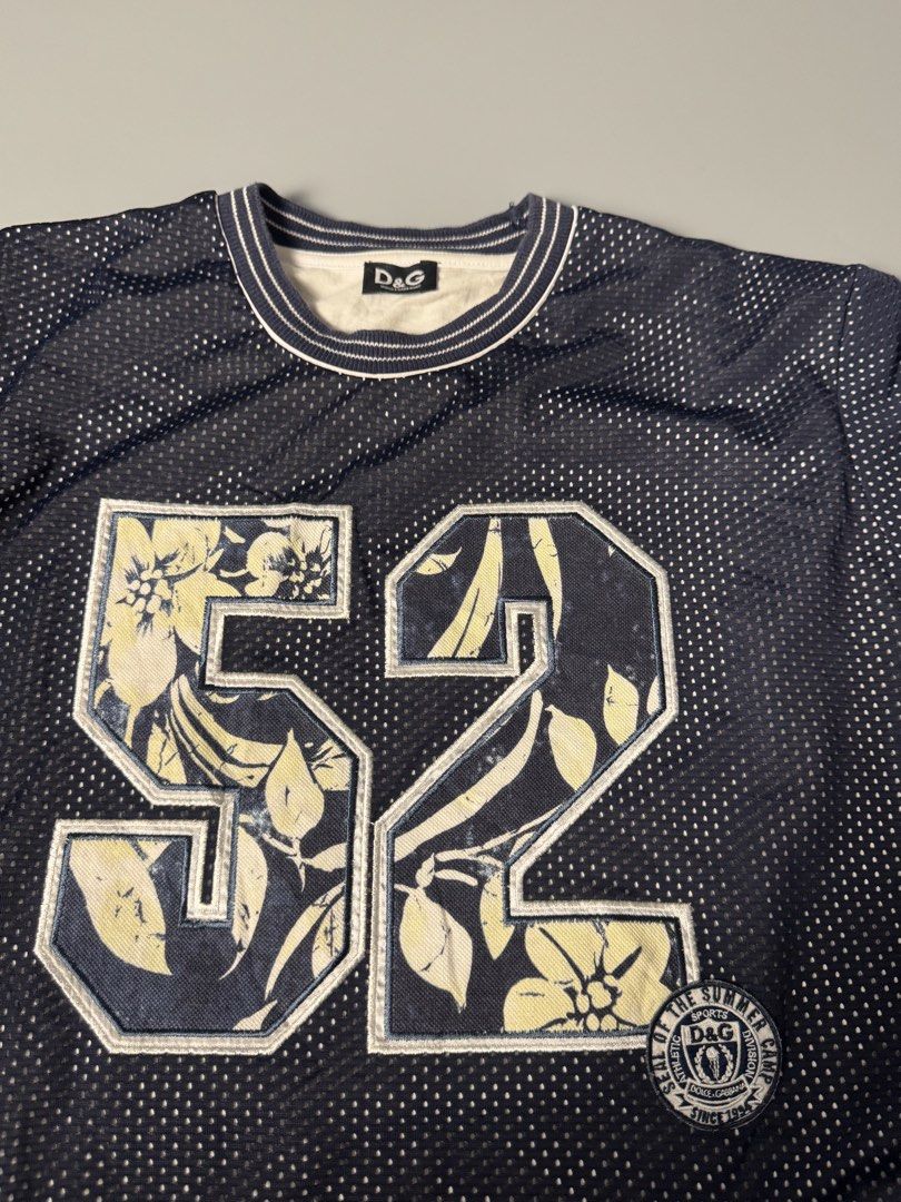 D&G Dolce & Gabbana Mesh Jersey 52 (Category: Tshirts & Polo Shirts ) located in San Pedro. Submitted by ygthriftshop (Listing ID 1469661030, Image 2). Description: - 21 x 27 - Brand: D&G Dolce & Gabbana - Style: Dark blue mesh jersey with white contrast ribbing on collar and cuffs - Graphic: Large number 52 on front filled with a stylish floral pattern - Fit/Size: Tagged Size L with an adjustable drawstring hem for a custom fit - Comfort: Featur