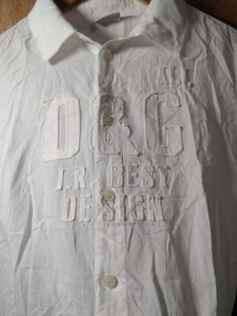 D&G Junior White Button-Up Shirt (Category: Shirts) located in Baguio. Submitted by tabuzomaria1422 (Listing ID 1469699983, Image 2). Description: - Brand: D&G Junior - Color: Classic White - Style: Short-sleeve button-up shirt - Design: Large embroidered D&G logo lettering on the chest - Details: Branded buttons down the front and collar neckline - Origin: Made in Turkey - Care: Wash and iron inside out (tag instructions included) Need Wash Only