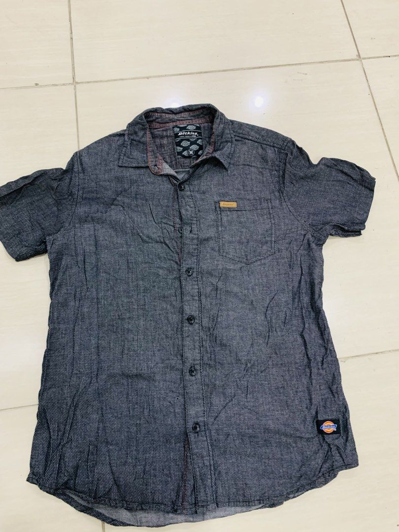 Dickies Short Sleeve Button Down Shirt Size M (Category: Tshirts & Polo Shirts ) located in Manila. Submitted by gizmolacaba (Listing ID 1469672679, Image 2). Description: - Brand: Dickies - Size: Medium (M) - Color: Dark grey with a subtle textured pattern - Style: Short sleeve, button-up front, regular collar - Details: Chest pocket with leather logo patch and classic woven logo tag near the bottom hem - Condition: Great casual piece for everyd