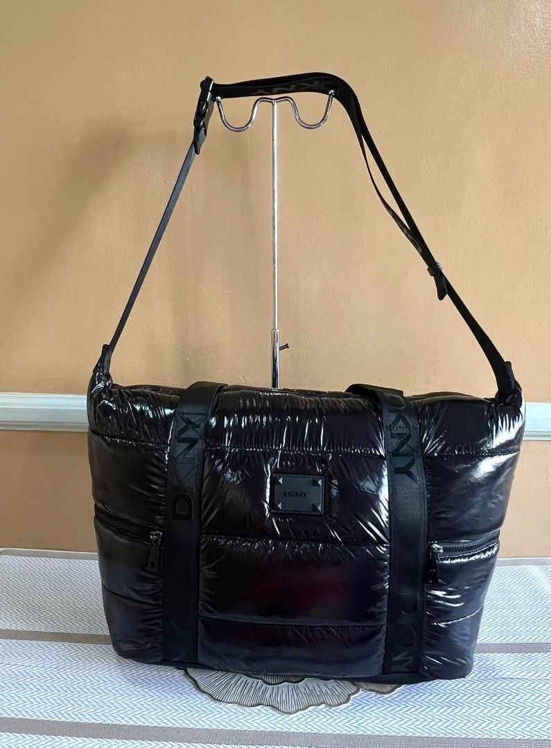 DKNY Black Puffer Tote Bag with Shoulder Strap (Category: Tote Bags) located in Quezon City. Submitted by bellafashion08 (Listing ID 1469731288, Image 3). Description: - Brand: DKNY Dimension: - Height = 12 in. - Length = 14 in. * From U.S * Nice in actual - Material: 100% Nylon with PU trim (Mfg Date: August 2021) - Design: Puffy glossy finish with branded black webbed straps - Storage: Spacious interior with dark patterned lining and front zipp