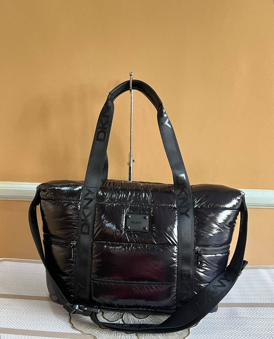 DKNY Black Puffer Tote Bag with Shoulder Strap (Category: Tote Bags) located in Quezon City. Submitted by bellafashion08 (Listing ID 1469731288, Image 1). Description: - Brand: DKNY Dimension: - Height = 12 in. - Length = 14 in. * From U.S * Nice in actual - Material: 100% Nylon with PU trim (Mfg Date: August 2021) - Design: Puffy glossy finish with branded black webbed straps - Storage: Spacious interior with dark patterned lining and front zipp