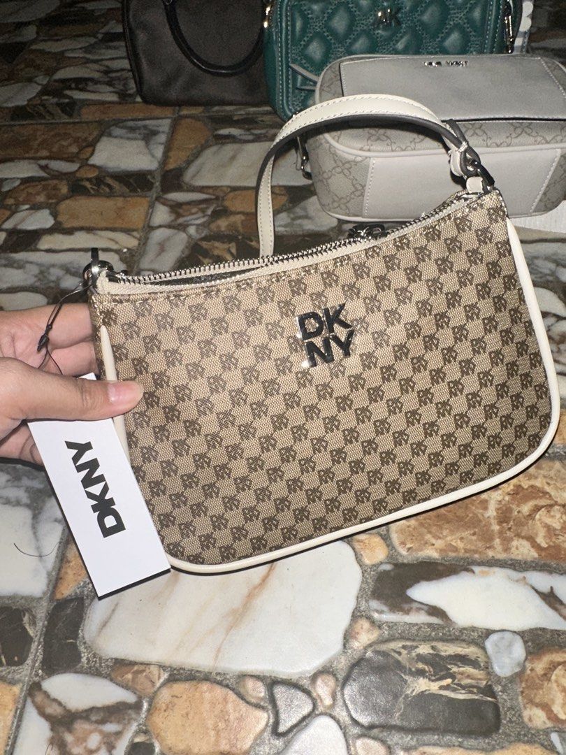 DKNY Monogram Shoulder Bag (Category: Luxury Bags & Wallets) located in Bugallon. Submitted by lavenderlane (Listing ID 1469669275, Image 2). Description: - Brand: DKNY - Style: Monogram shoulder bag - Color: Brown with white trim - Hardware: Silver-tone with zip top closure - Interior: Black fabric lining with a zippered pocket and brand patch - Condition: Brand new with original hang tag attached - Size: Compact, ideal for daily essentials.