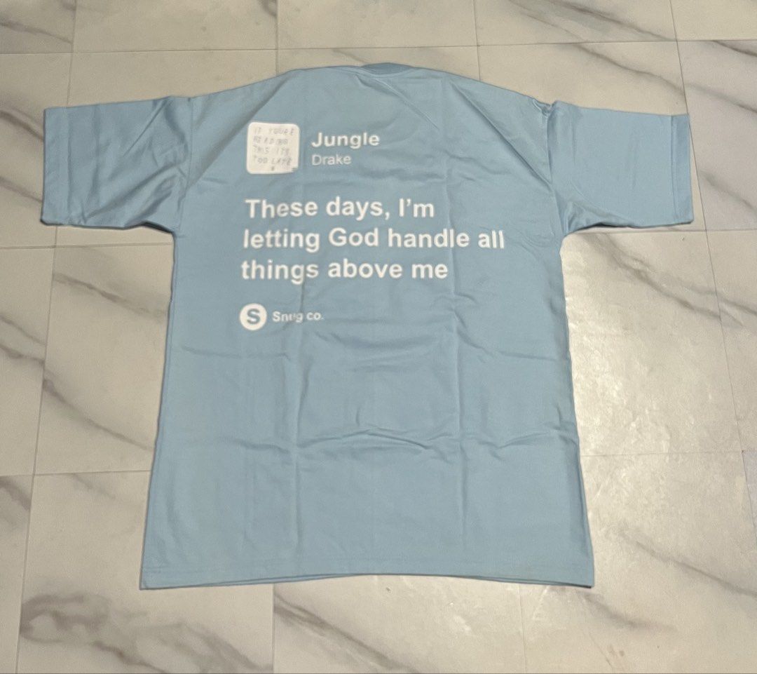 Drake Graphic Tee Light Blue (Category: Tshirts & Polo Shirts ) located in Cavite. Submitted by christianzuuu (Listing ID 1469739116, Image 3). Description: - Brand: Snug Co. - Color: Light blue - Design: Drake CLB graphic on front, 'Jungle' lyrics and song info on back - Material: Heavy cotton - Fit: Relaxed fit - Measurements: 21 inches (width) x 27 inches (length) - Condition: Clean, no stains or flaws.