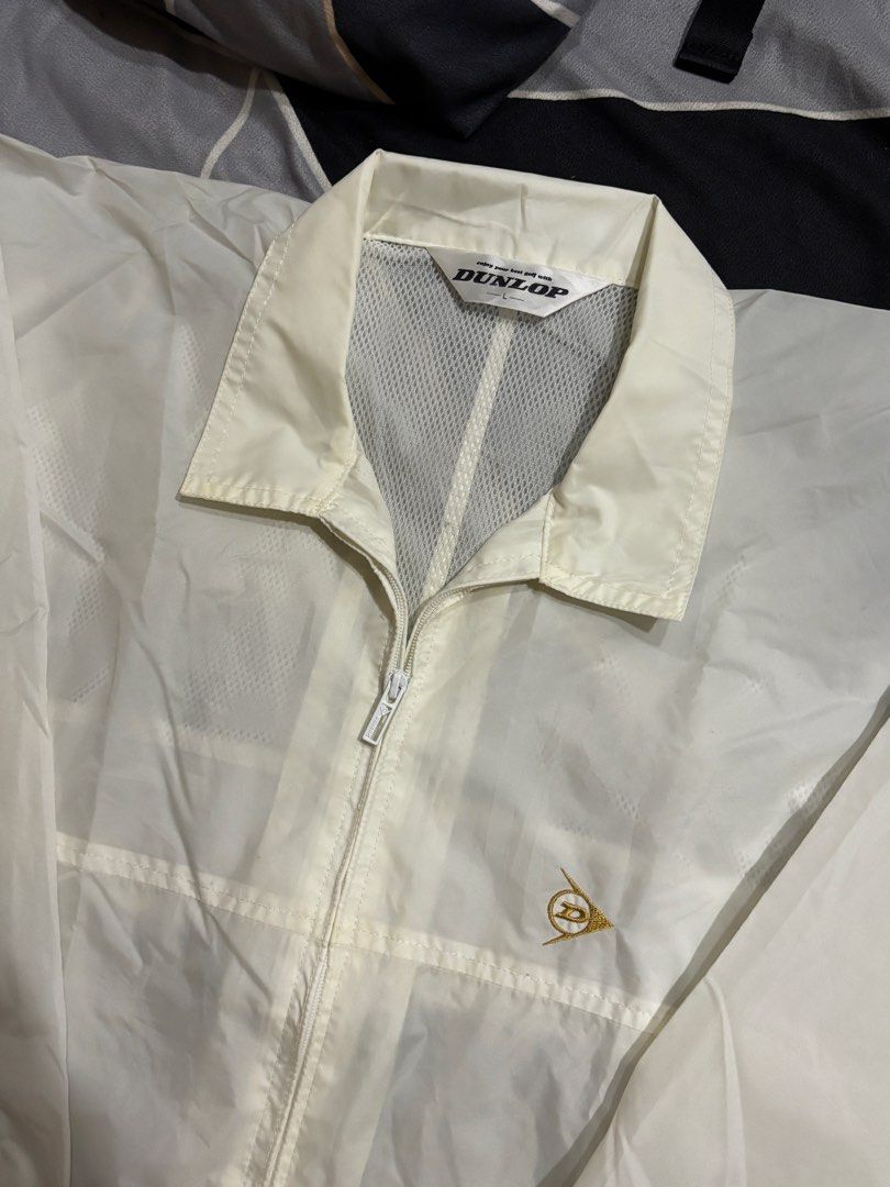 Dunlop Windbreaker Jacket (Category: Coats, Jackets and Outerwear) located in Manila. Submitted by bizcuits (Listing ID 1469739511, Image 3). Description: - Brand: Dunlop - Color: Off White - Size: Large (L) 23 width by 30 length - Design: Full front zip with fold-down collar and small gold embroidered chest logo - Features: Front pockets, drawstring hem, and breathable mesh lining - Condition: Great lightweight outer layer, ideal for breezy days