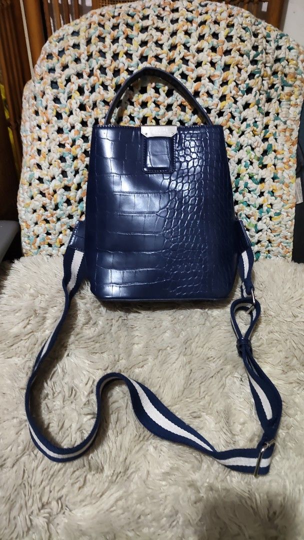 Esquire Blue Crocodile Print Handbag/sling bag (Category: Shoulder Bags) located in Cebu City. Submitted by lumaynojes00490 (Listing ID 1469671406, Image 1). Description: - Color: Dark blue with a glossy finish - Design: Mixed crocodile-embossed and smooth leather texture - Hardware: Silver-tone with a secure clasp detail - Straps: Short top handle + adjustable navy and white striped canvas strap - Capacity: Spacious interior, perfect for everyda