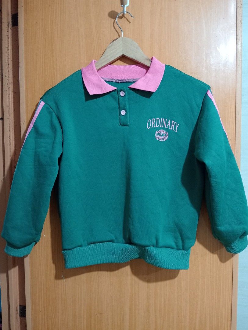 Green pink Ordinary polo sweatshirt (Category: Longsleeves) located in Quezon City. Submitted by niceoutfits (Listing ID 1469715657, Image 2). Description: - Color: Green with pink accents - Age : 10 yr old - Design: Pink polo collar, sleeve stripes, chest text, and circular crest graphic - Closure: Two-button placket at the neckline - Details: Ribbed cuffs and hem for a snug fit - Interior: Soft, warm fleece fabric inside - Condition: Brand new 