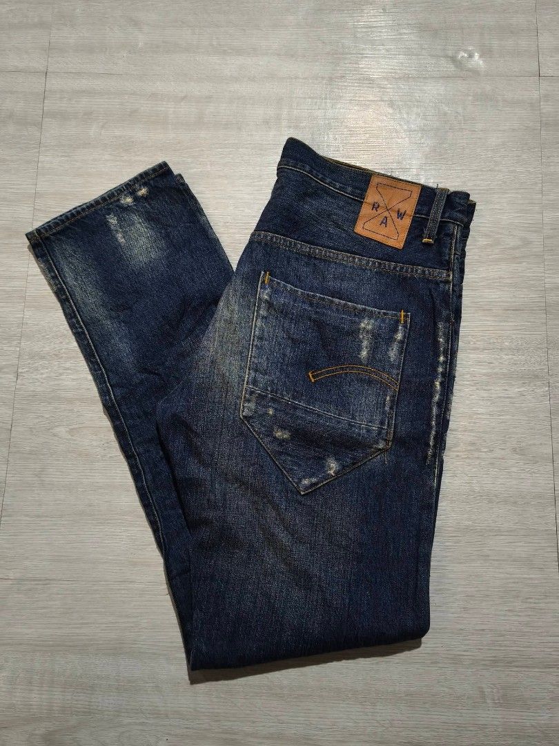 G-Star RAW Distressed Denim Jeans (Category: Jeans) located in General Tinio. Submitted by mariyaspreloved (Listing ID 1469589548, Image 3). Description: - Brand: G-Star RAW - Wash: Dark blue denim - Closure: Button fly with branded metal buttons - Details: Distressed look with patched right knee tear and frayed cuffs - Branding: Distinctive leather patch on back waistband - Pockets: Classic five-pocket styling with unique angled back pockets -si