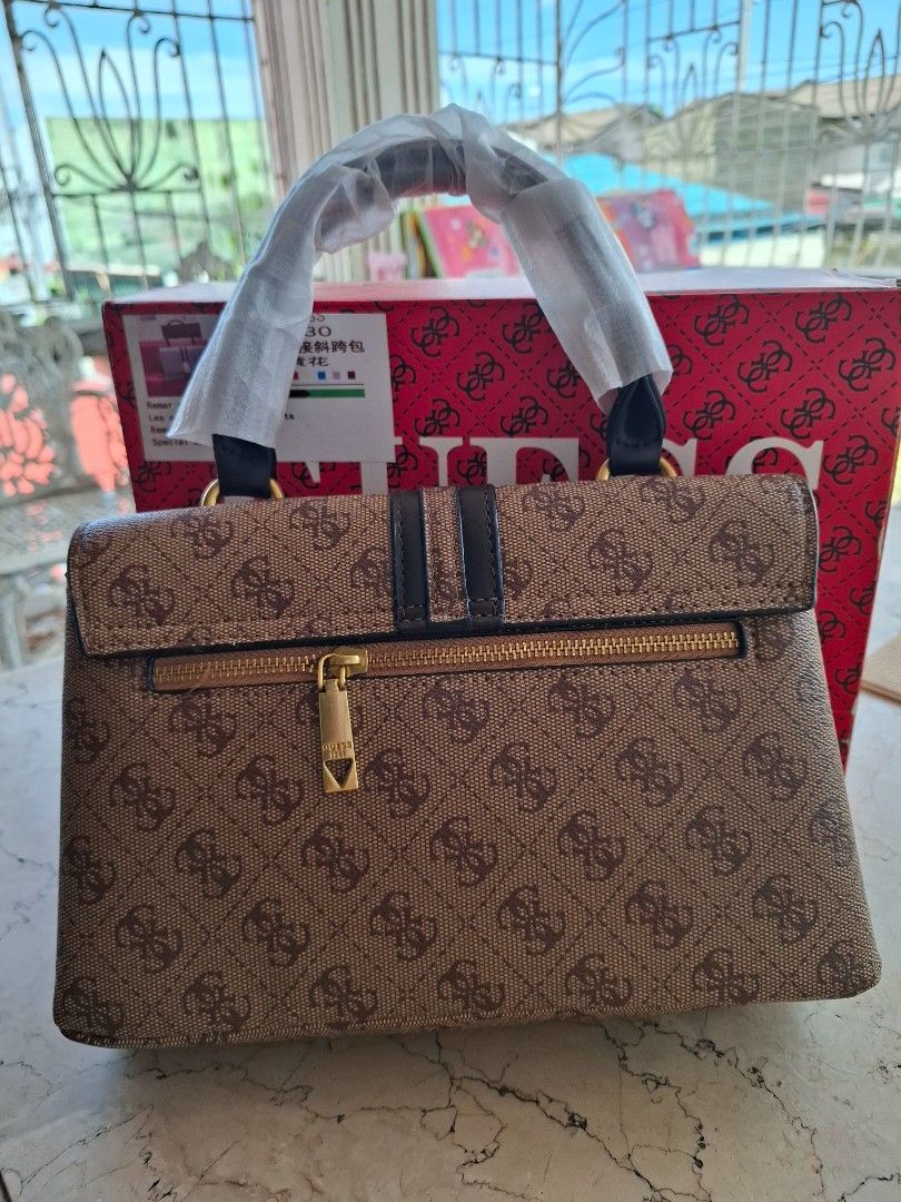 Guess Monogram Brown Top Handle Handbag With Sling (Category: Luxury Bags & Wallets) located in Manila. Submitted by jujutwo (Listing ID 1469610895, Image 2). Description: - Classic brown monogram print with elegant dark brown panels - Luxurious gold-tone hardware and back zipper pocket - Firm, structured shape that maintains form - Handles still wrapped in original protective plastic - Brand new and includes a matching branded gift box.