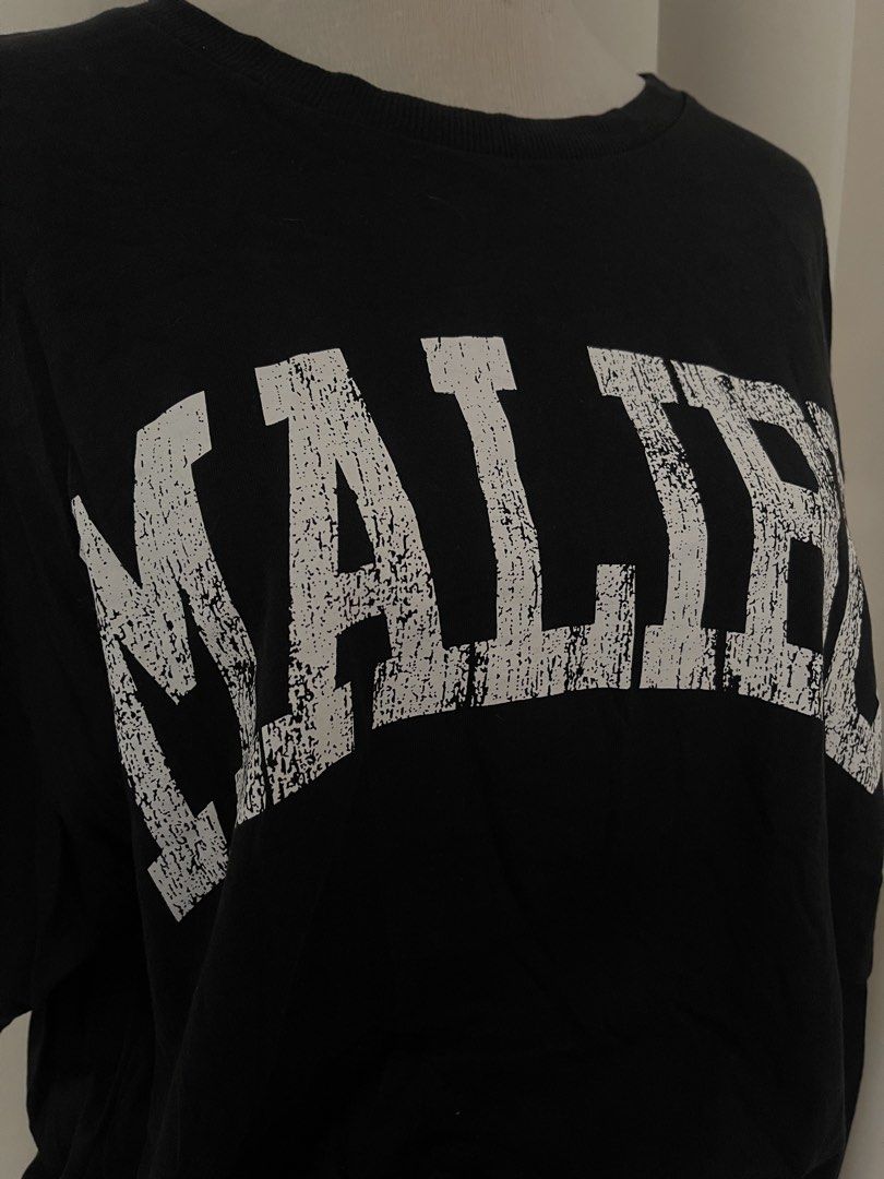 H&M Divided Black Malibu (Category: Shirts) located in Cainta. Submitted by zlove111 (Listing ID 1469620304, Image 3). Description: - Brand/Model: H&M Divided - Color: Black with white distressed 'Malibu' collegiate graphic - Fit: Relaxed, oversized fit with crew neckline - Size: Medium (tag attached) up to xl boxy 23" - Material: Soft and comfortable cotton - Styling: Easy to pair with denim jeans or shorts for a casual streetwear look not faded