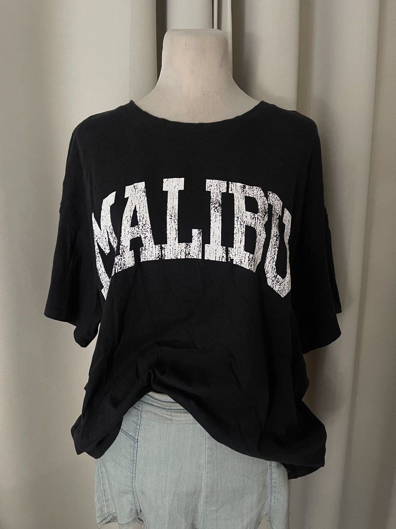 H&M Divided Black Malibu (Category: Shirts) located in Cainta. Submitted by zlove111 (Listing ID 1469620304, Image 2). Description: - Brand/Model: H&M Divided - Color: Black with white distressed 'Malibu' collegiate graphic - Fit: Relaxed, oversized fit with crew neckline - Size: Medium (tag attached) up to xl boxy 23" - Material: Soft and comfortable cotton - Styling: Easy to pair with denim jeans or shorts for a casual streetwear look not faded