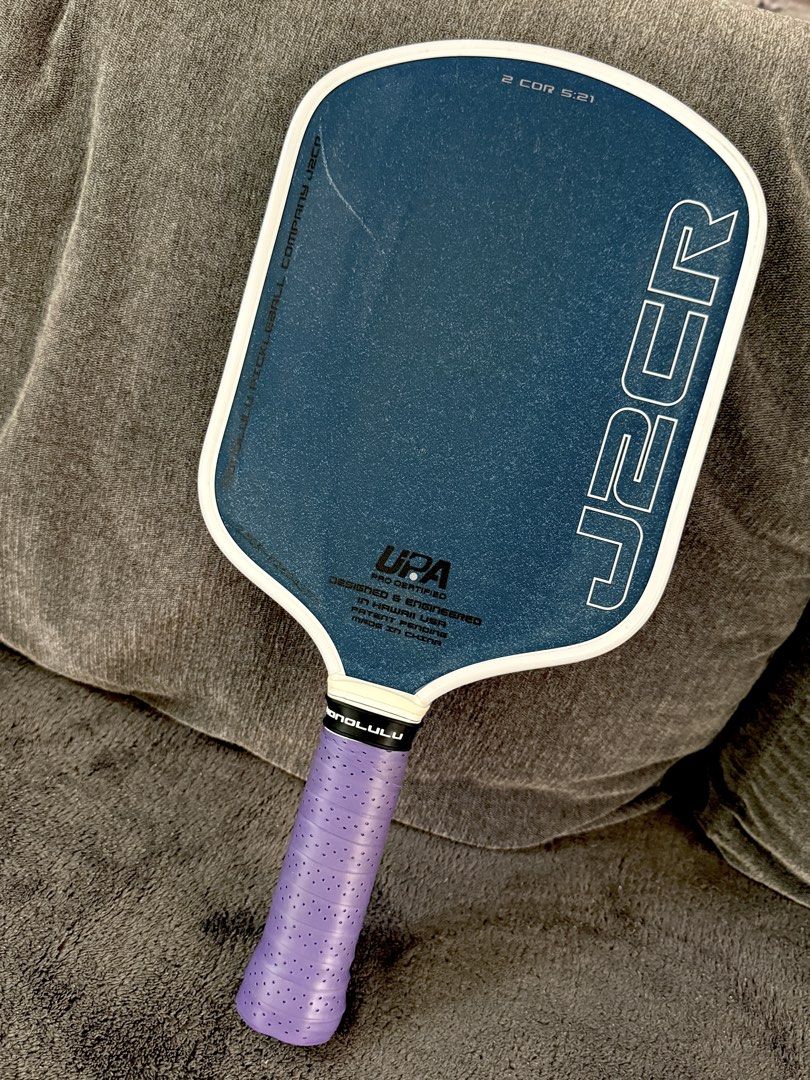 Honolulu Pickleball Company J2CR Paddle (Category: Racket and Ball Sports) located in Taguig. Submitted by sandz392 (Listing ID 1469717207, Image 1). Description: - Brand/Model: Honolulu Pickleball Company J2CR paddle in blue - Grip: Upgraded with a purple perforated overgrip, standard grip band intact - Authenticity: White edge guard with Honolulu branding and official authentication sticker near the throat - Condition: Ready for the courts.
