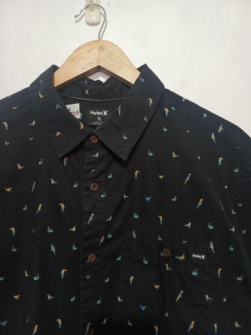 HURLEY PARROT SHIRT (Category: Tshirts & Polo Shirts ) located in Baguio. Submitted by 074thriftmania (Listing ID 1469692754, Image 2). Description: - Brand: Hurley - Style: Short sleeve button-up shirt - Color/Design: Black with colorful all-over parrot and floral print - Features: Collared neckline, brown front buttons, single chest pocket with logo tag - Size: XL - Measurements: 23.5 inches pit-to-pit, 29.5 inches length.