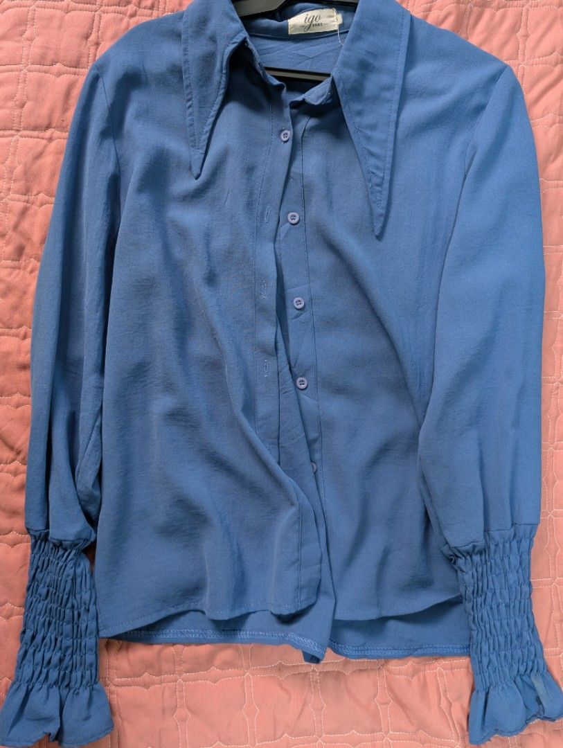 Igo Blue Long Sleeve Button Up Blouse (Category: Longsleeves) located in Manila. Submitted by deniniii (Listing ID 1469625266, Image 1). Description: - Brand: Igo - Color: Blue - Style: Long sleeve button-up shirt with sharp pointed collar - Details: Unique smocked ruffled cuffs at the wrists - Fabric: Lightweight and smooth finish - Versatility: Great for casual wear or dressing up Can fit up to large.