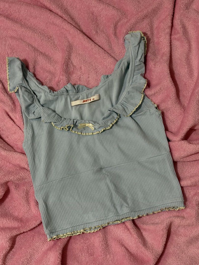 Just G Blue Ruffled Ribbed Tank Top (Category: Sleeveless) located in Nagcarlan. Submitted by nkkva (Listing ID 1469690095, Image 1). Description: - Brand/Model: Just G - Size: Medium - Color: Light blue with contrast yellow stitching - Details: Wide scoop neck, ruffled lettuce trim edges, and a small cream bow in front - Fit: Cropped - Style: Great basic piece to pair with high-waisted denim or skirts.
