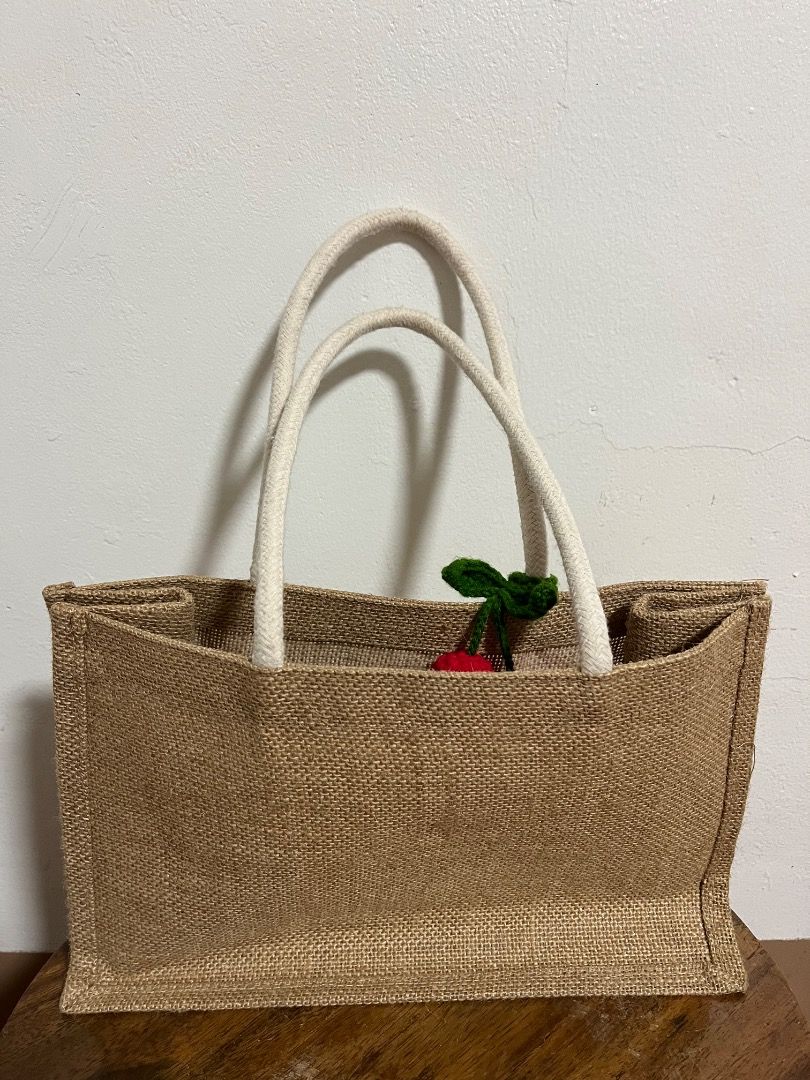 Jute Tote Bag with Crochet Cherry Charm (Category: Tote Bags) located in Cabuyao City. Submitted by rdtrmt (Listing ID 1469666966, Image 2). Description: - Material: Durable neutral brown burlap with soft white fabric handles - Features: Includes a cute handmade crochet cherry charm on the strap - Design: Structured rectangular shape with a flat bottom - Capacity: Roomy interior for all your essentials - Best For: Daily use, grocery runs, and cas
