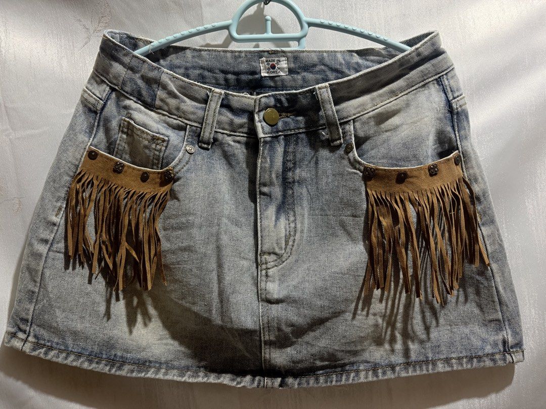 Korean denim fringe mini skirt (boho) (Category: Skirts) located in Liloan. Submitted by betchangel (Listing ID 1469727093, Image 1). Description: - Style: Western Boho denim mini skirt - Origin: Made in Korea - Wash: Light wash denim - Details: Brown faux suede front pockets with long fringe and metal studs - Closure: Button closure and zipper fly - Features: Built-in belt loops - Pairing: Easy to style with boots or sneakers.